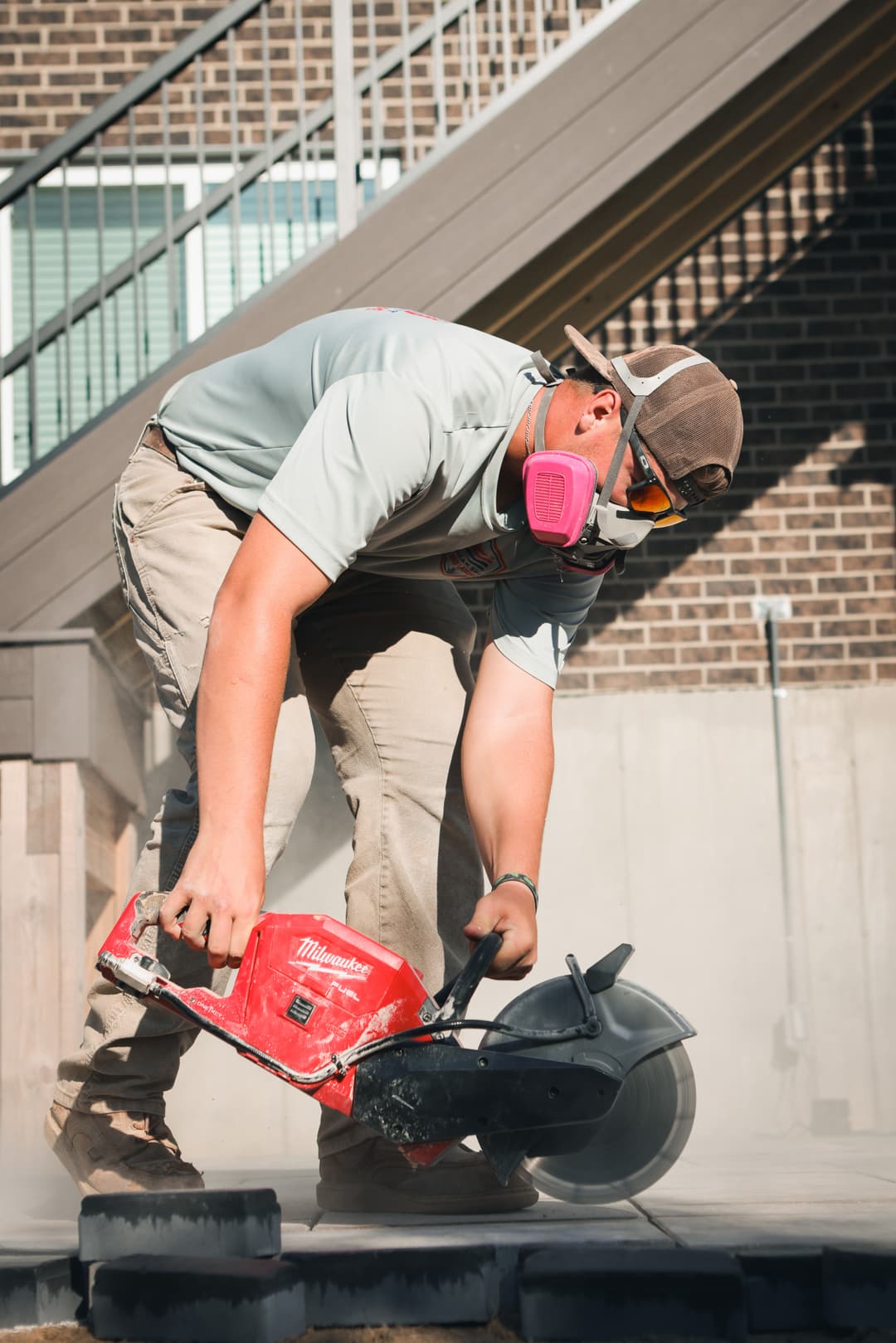 Construction worker cutting stone with a power saw, wearing safety gear and a dust mask.