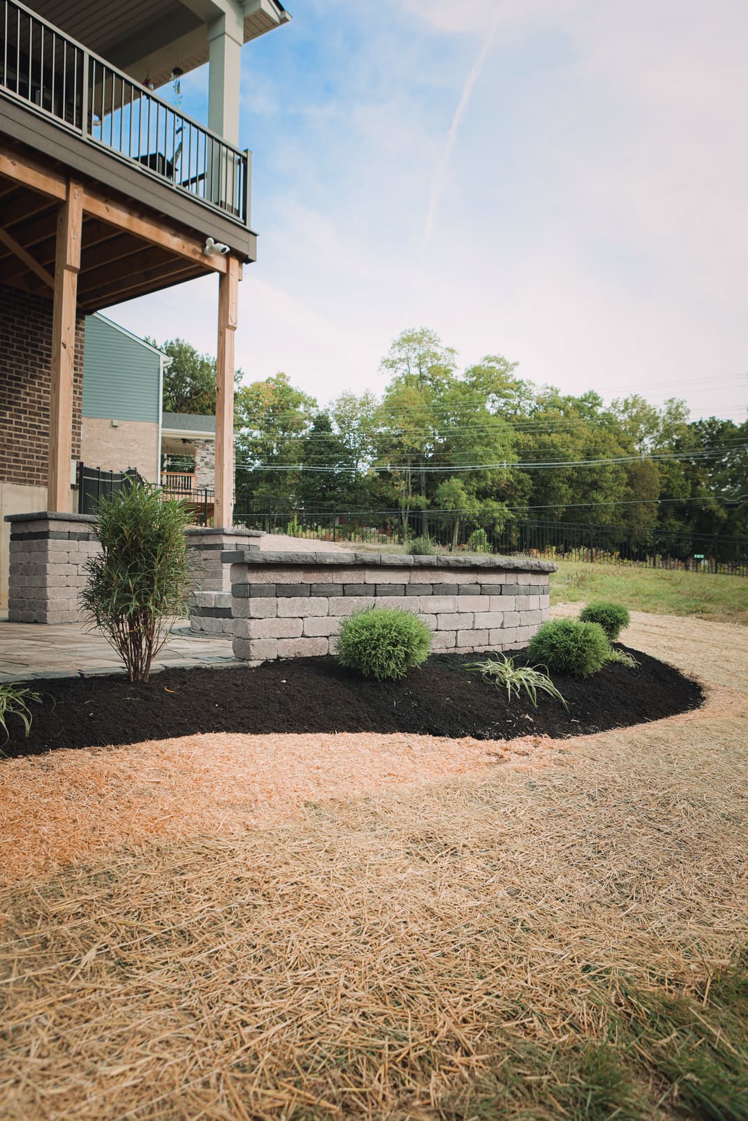 Backyard landscaping featuring stone wall, ornamental shrubs, and sod under a clear sky.