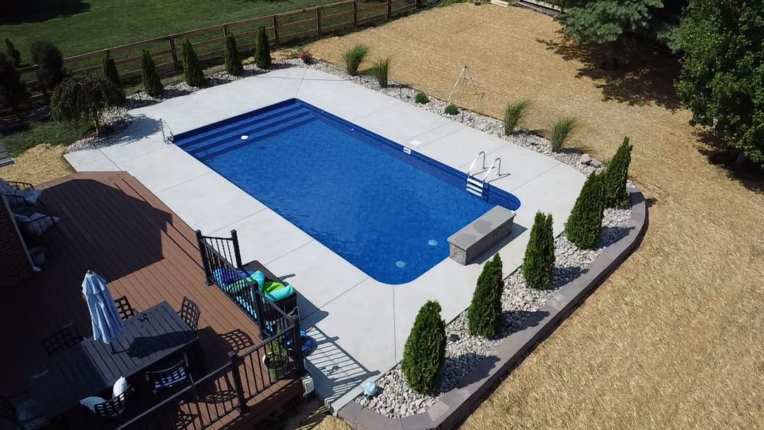 Aerial view of a modern backyard pool with landscaped surroundings and a wooden deck.