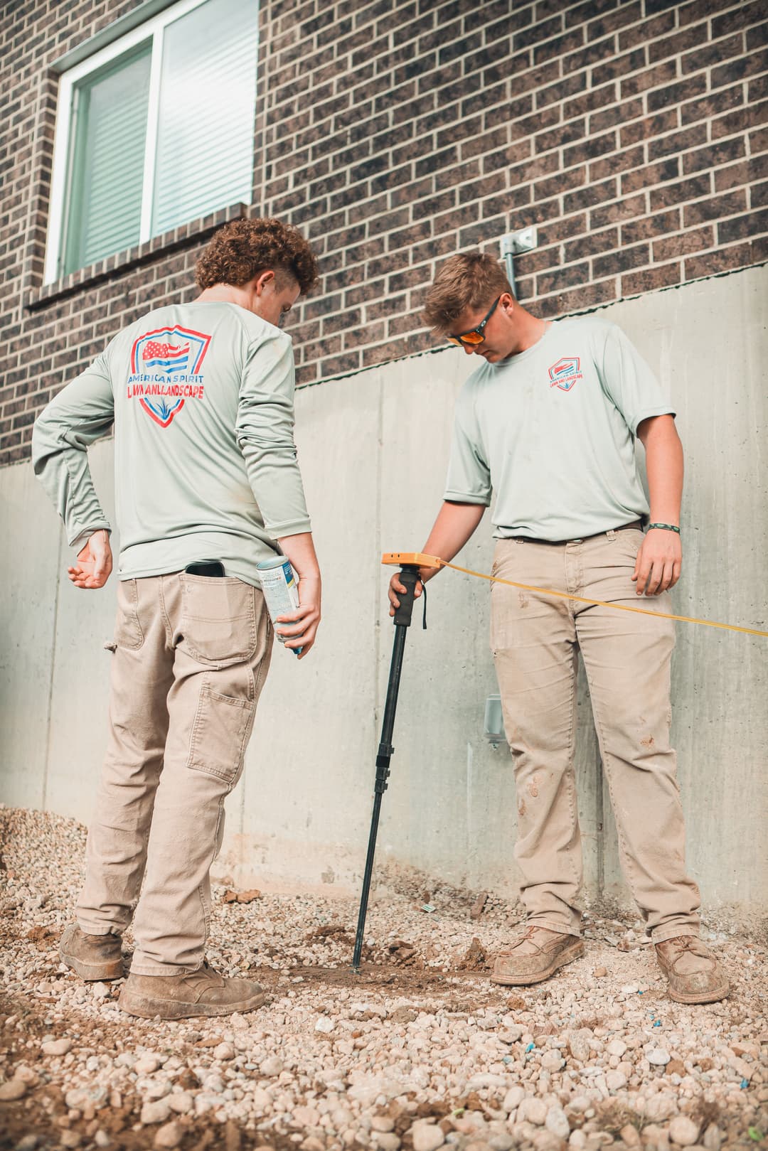Two workers in matching shirts using a tool to measure ground depth at a construction site.