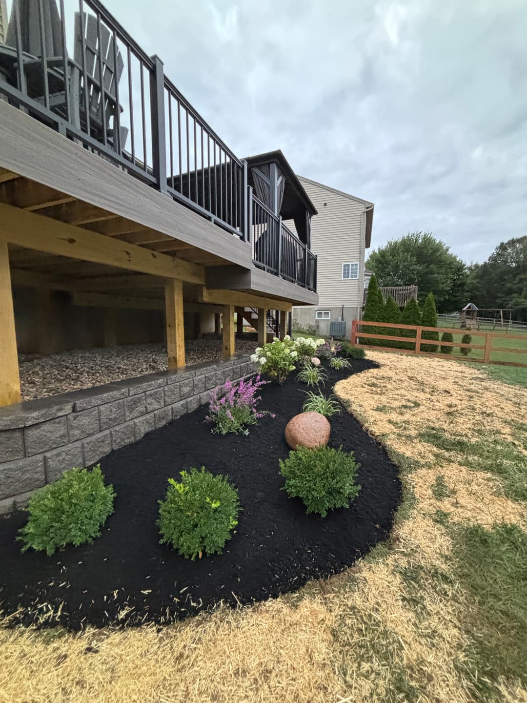 Beautifully landscaped yard with black mulch, shrubs, and a deck overlooking the garden.