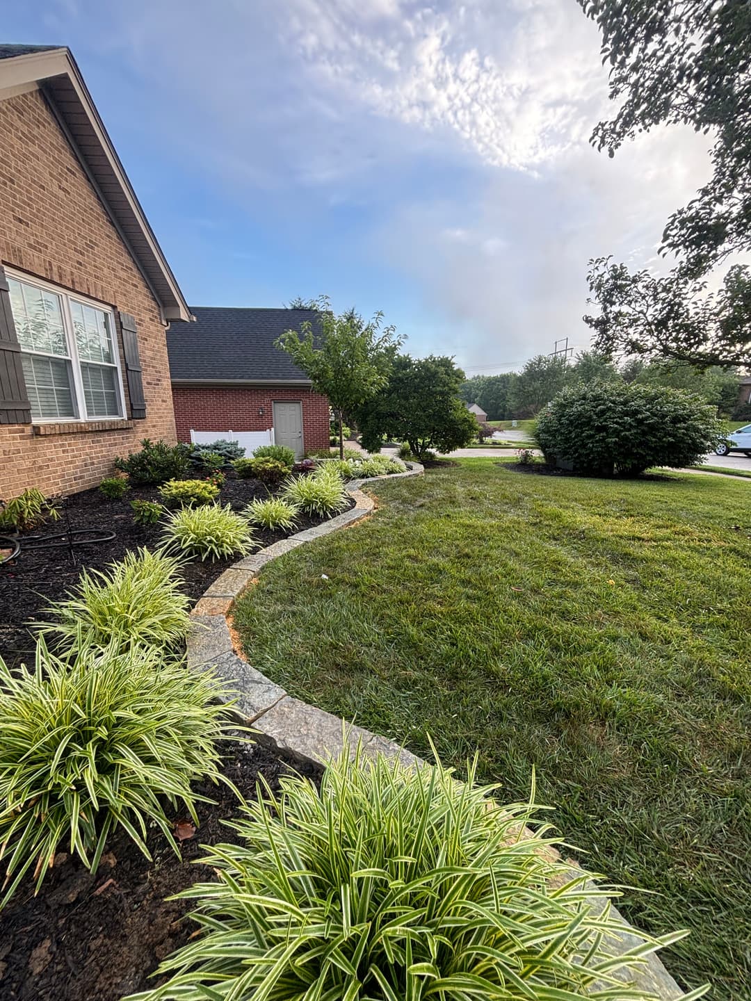 Lush landscaping with stone path, colorful plants, and house under a clear sky.