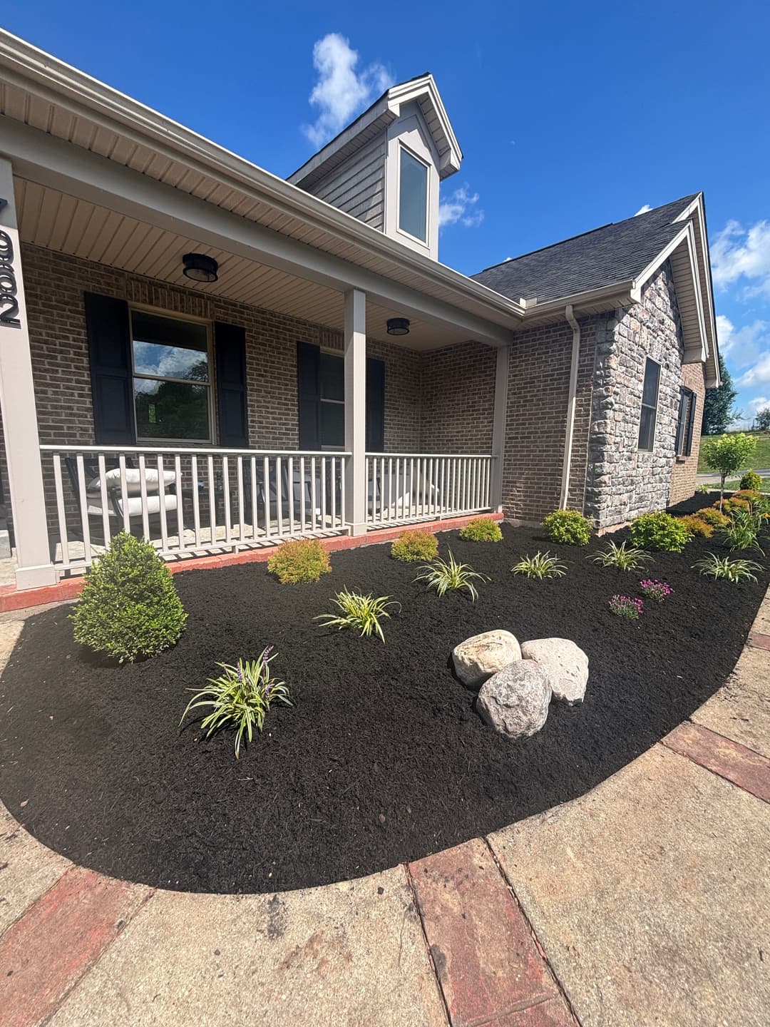 Well-maintained home exterior with landscaped garden featuring mulch, shrubs, and stones.