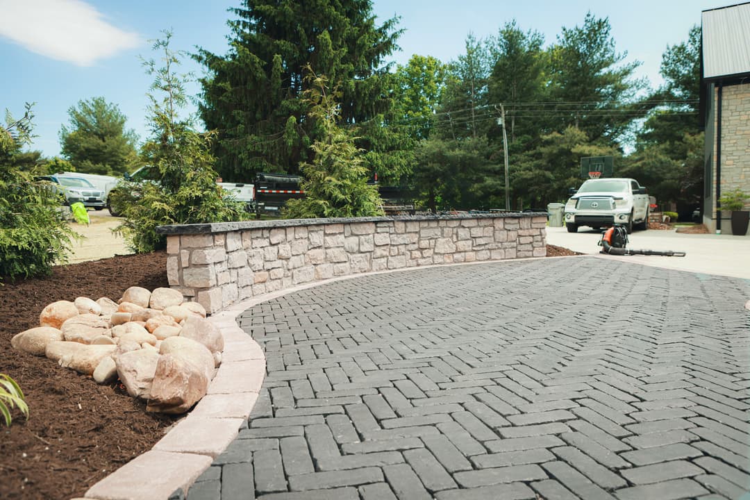 Paved Walkway with stone wall, landscaping rocks, and workers in background.
