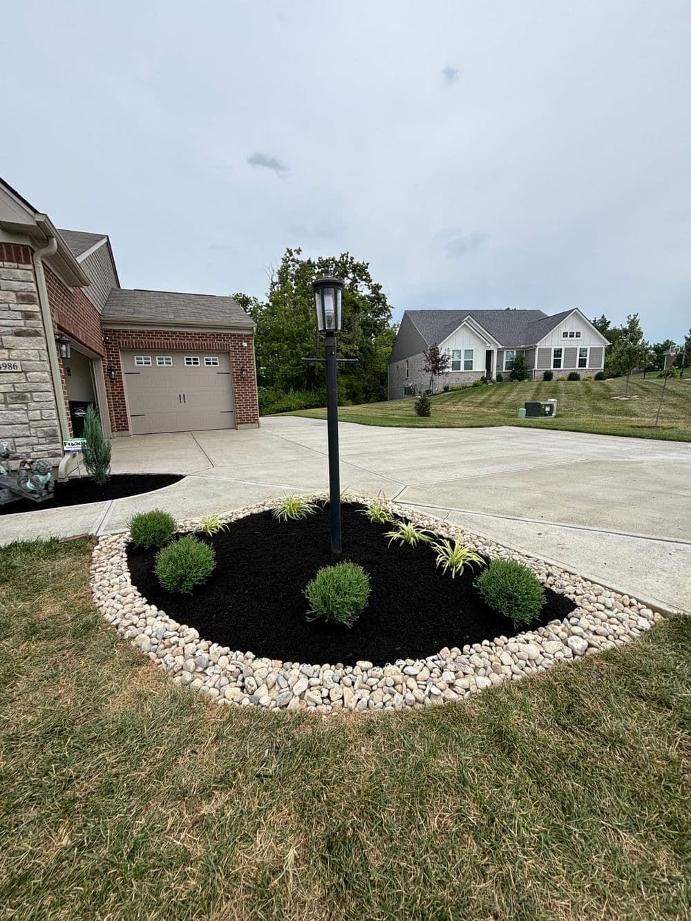 Landscape design featuring a black mulch garden with a lantern and rounded stone border.