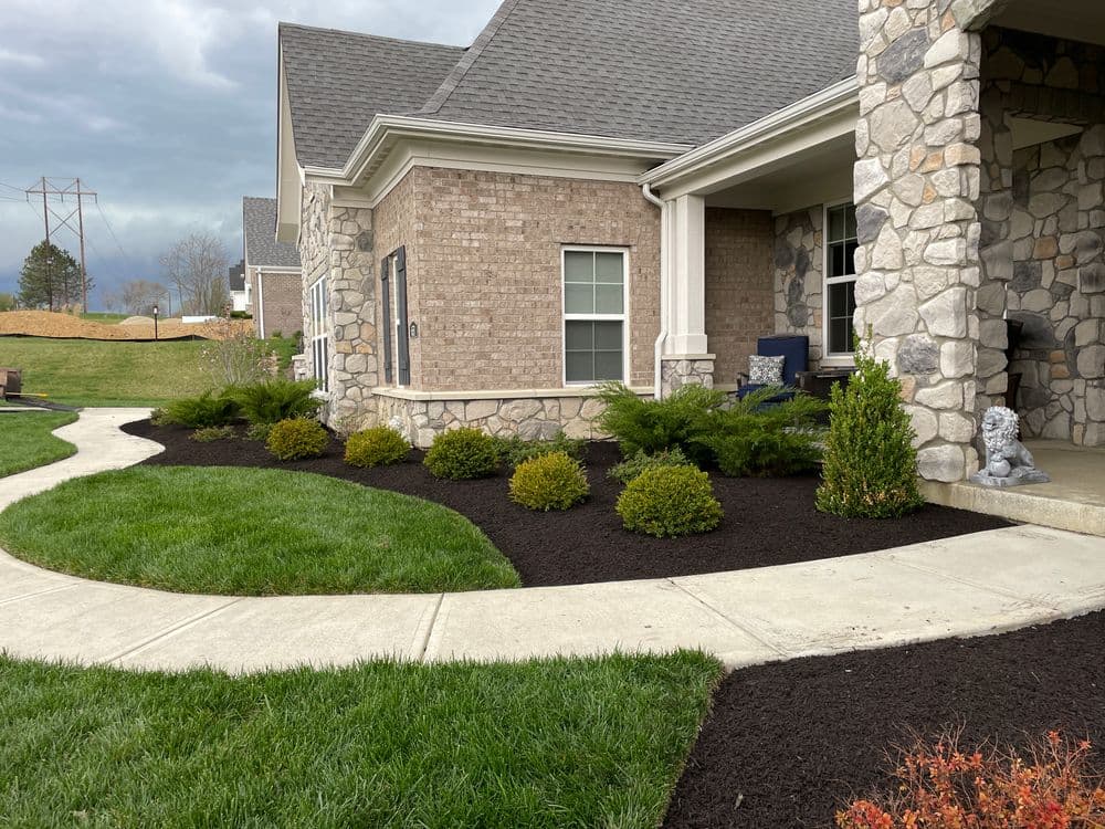 Landscaped home entrance with stone siding, curving walkway, and manicured shrubs.