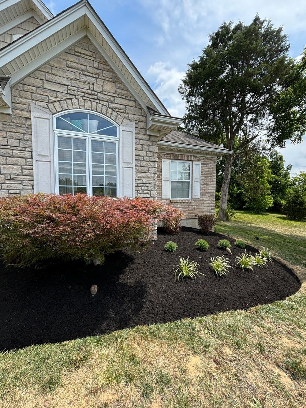 Stone house exterior with landscaped garden featuring shrubs and flower beds.