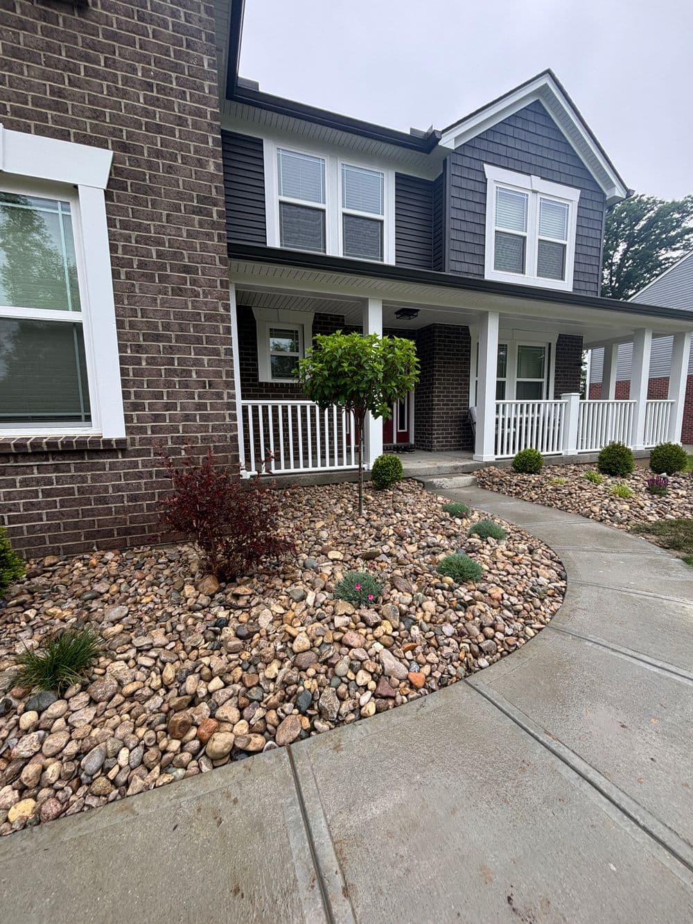 Front view of a modern home with brick exterior, landscaped rocks, and green shrubs.