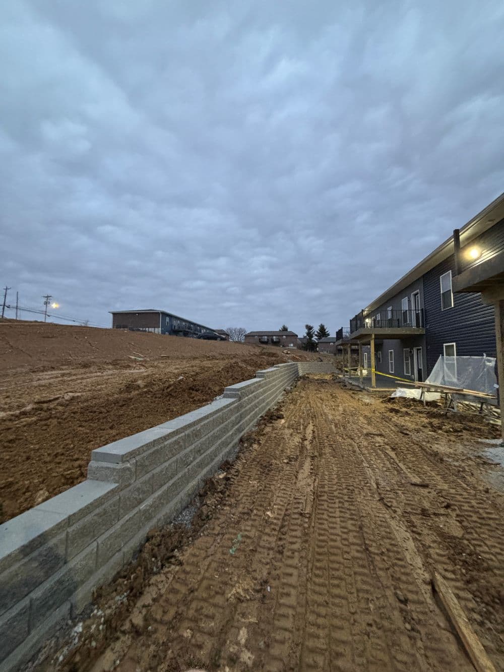Construction site with a concrete wall, gravel path, and overcast sky in the background.