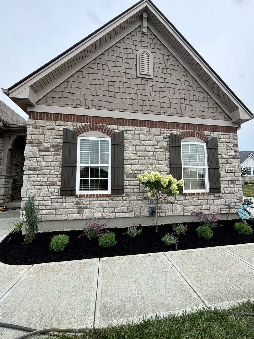 Modern home exterior with stone and brick facade, landscaped garden, and flowering plants.