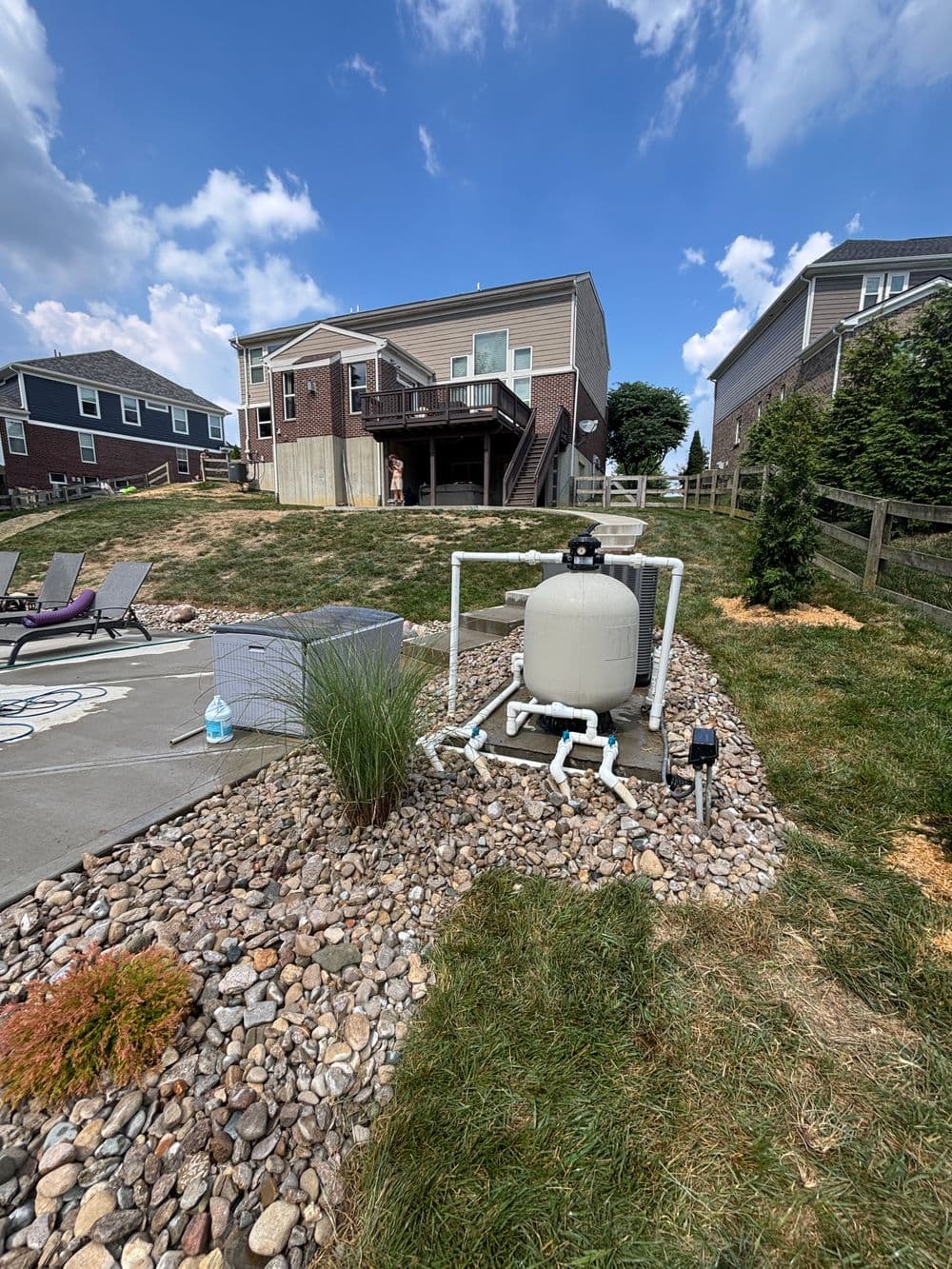 Residential backyard with a pool filtration system and landscaped rocks under a blue sky.