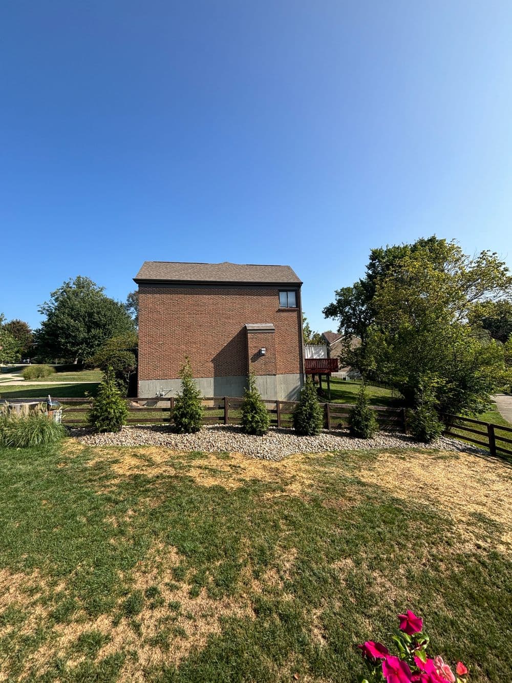 Two-story brick house with a clear blue sky, surrounded by greenery and landscaping.