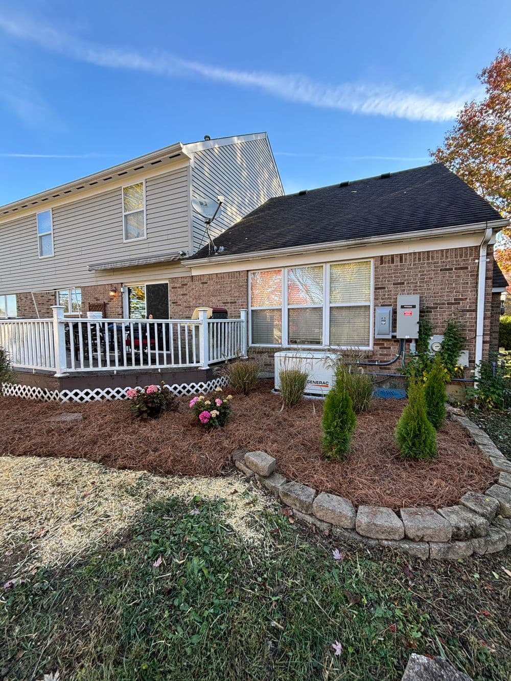Backyard view of a house with a deck, flower beds, and landscaped garden features.