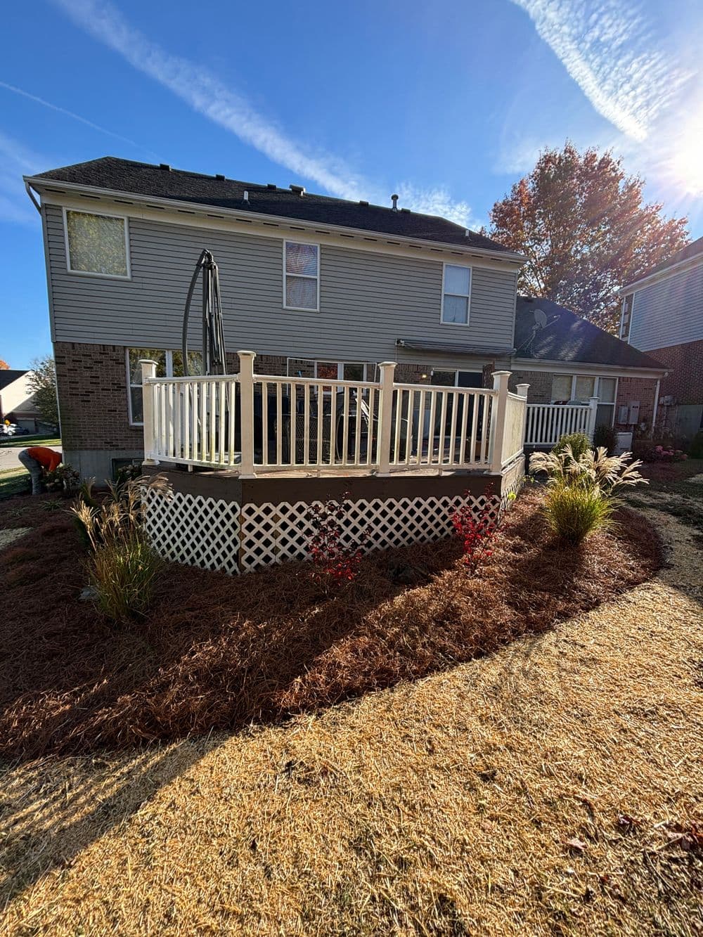 House with a spacious deck, landscaped yard, and vibrant autumn foliage in sunlight.