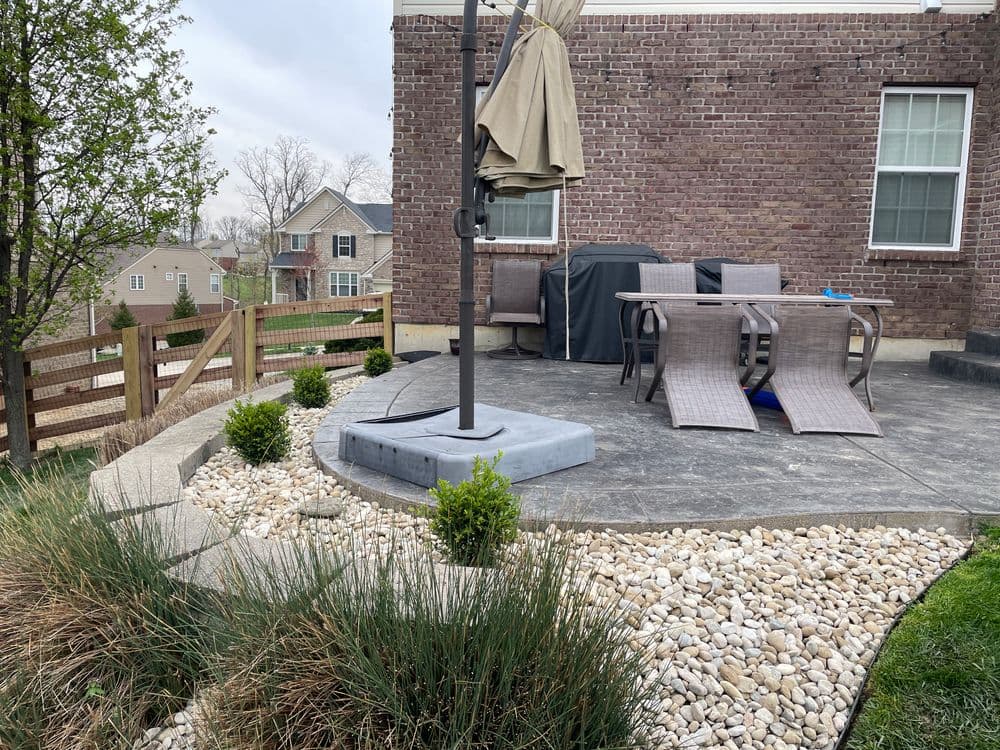 Patio with outdoor furniture and umbrella, bordered by landscaped stones and greenery.
