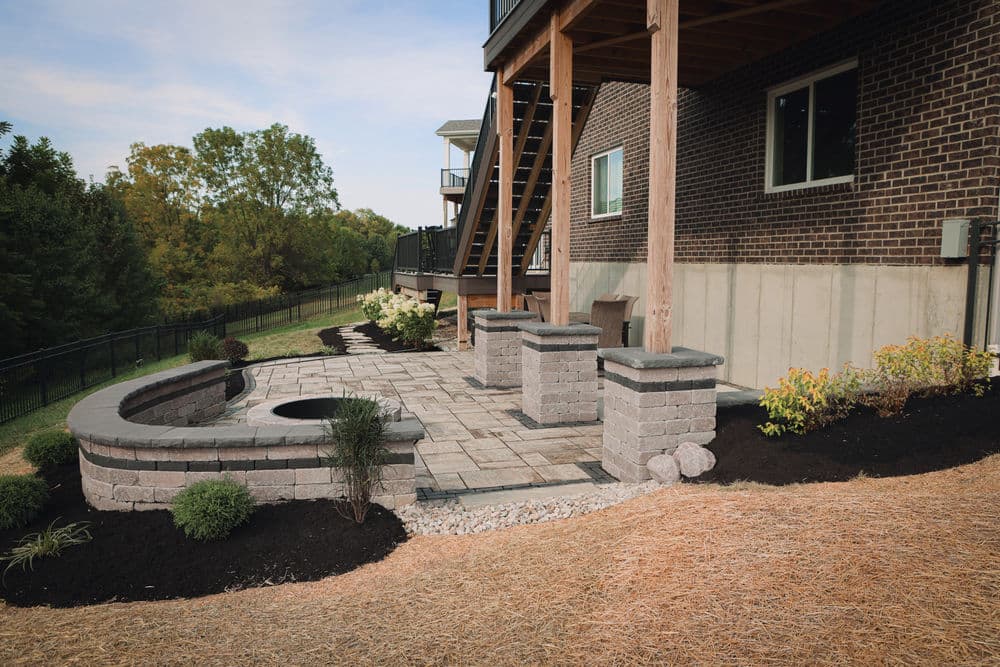 Outdoor patio design with stone seating, fire pit, and landscaped garden under a home's deck.